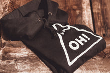 close up of Folded black hoodie with white triangle chest print and OH! lettering in the centre on wood decking