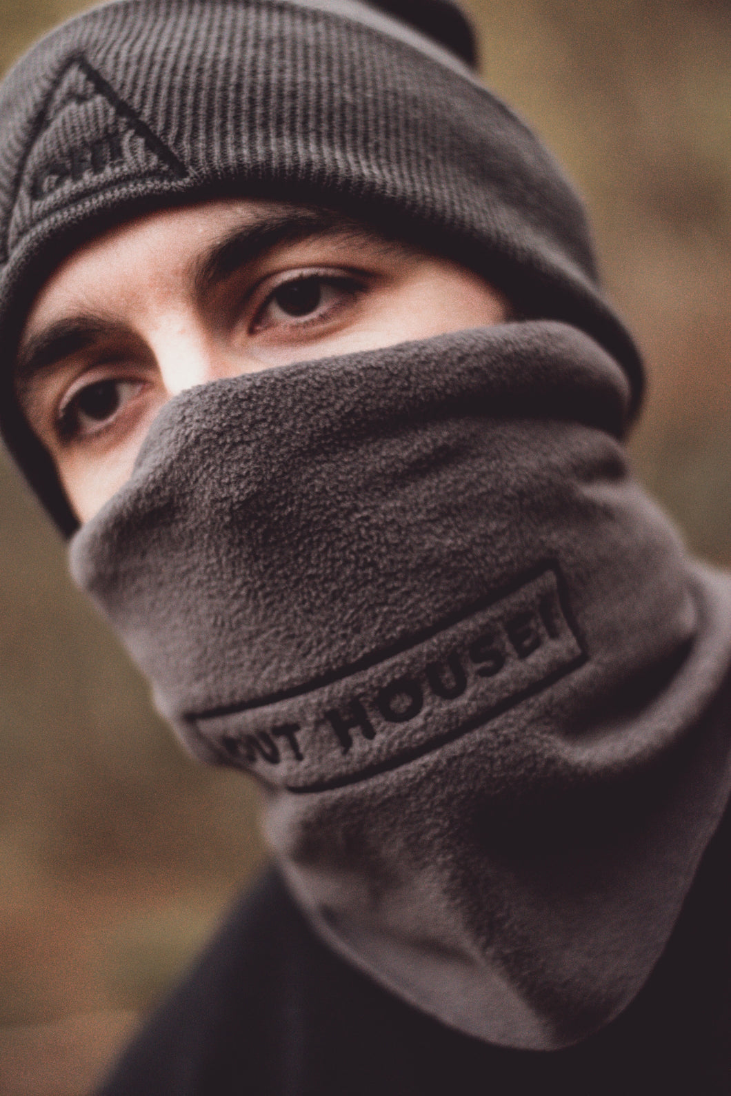 Angled view of Model wearing Grey snood with black OUT HOUSE! lettering and accompanying grey beanie to match 